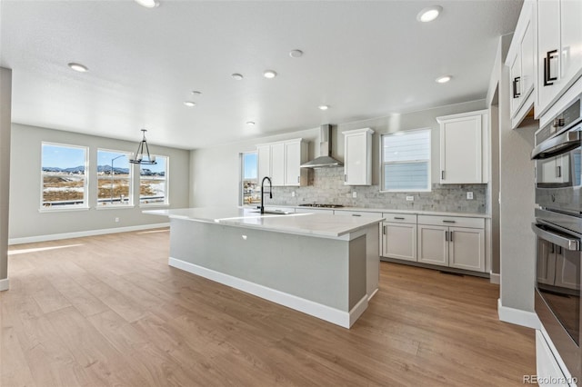 kitchen featuring white cabinetry, decorative light fixtures, an island with sink, and wall chimney exhaust hood