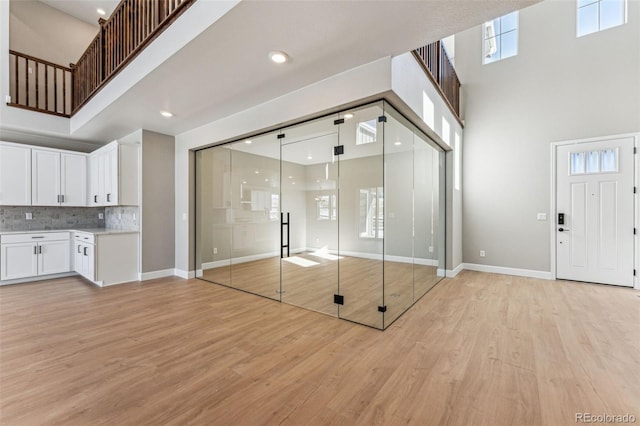 interior space with a healthy amount of sunlight, a high ceiling, light hardwood / wood-style flooring, and white cabinets