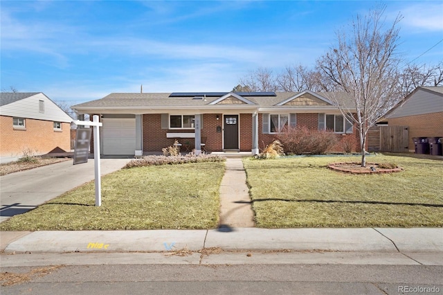 ranch-style home featuring brick siding, solar panels, a front yard, driveway, and an attached garage