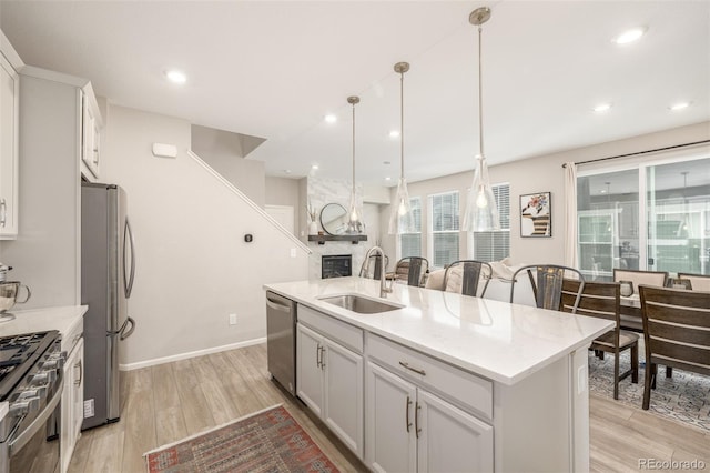 kitchen with appliances with stainless steel finishes, sink, pendant lighting, light hardwood / wood-style floors, and an island with sink