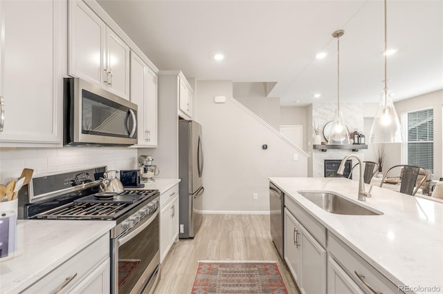 kitchen featuring sink, hanging light fixtures, stainless steel appliances, light hardwood / wood-style floors, and white cabinets