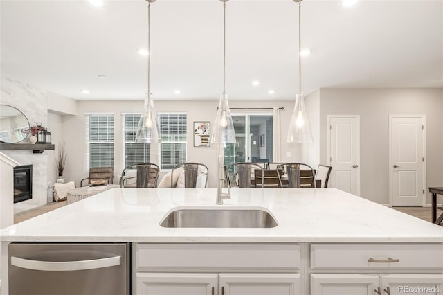 kitchen featuring a center island with sink, sink, light stone countertops, a fireplace, and white cabinetry