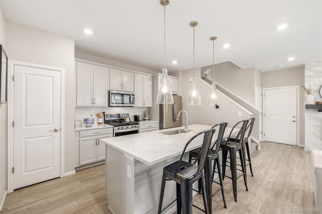 kitchen featuring appliances with stainless steel finishes, sink, pendant lighting, light hardwood / wood-style flooring, and white cabinets