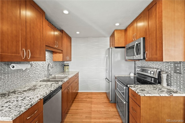 kitchen featuring light wood-style floors, stainless steel appliances, brown cabinetry, and a sink