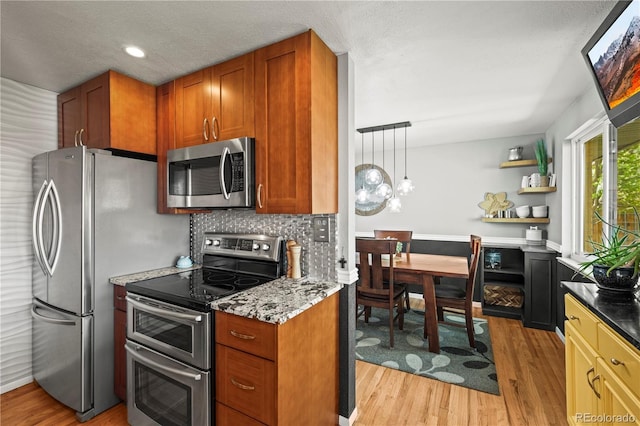 kitchen with light wood-style flooring, an inviting chandelier, backsplash, brown cabinets, and appliances with stainless steel finishes