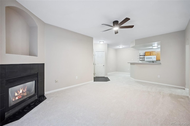 living room with light carpet, a tiled fireplace, and ceiling fan