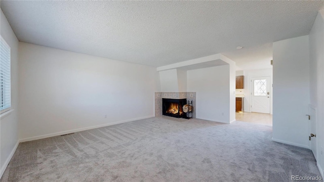 unfurnished living room featuring carpet flooring, a fireplace, a textured ceiling, and baseboards