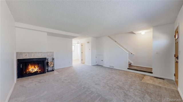 unfurnished living room with visible vents, stairway, a textured ceiling, carpet floors, and a fireplace