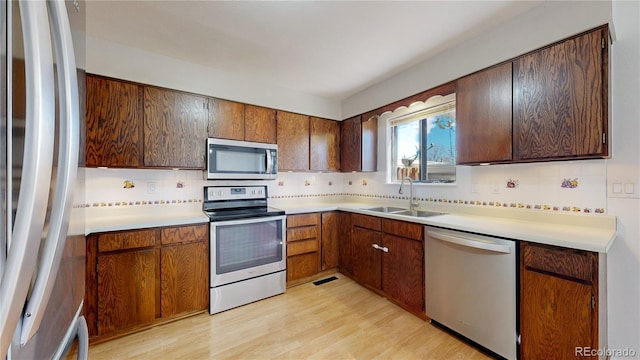 kitchen featuring light wood finished floors, tasteful backsplash, appliances with stainless steel finishes, light countertops, and a sink