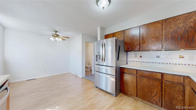 kitchen with light countertops, backsplash, appliances with stainless steel finishes, a textured ceiling, and light wood-type flooring