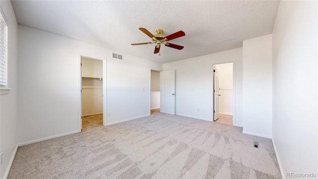 unfurnished bedroom with a textured ceiling, a spacious closet, visible vents, and baseboards