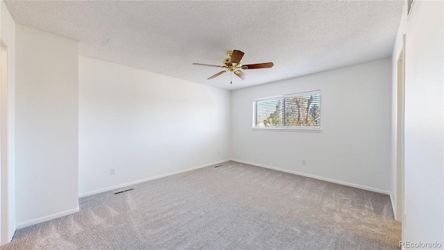 spare room with a textured ceiling, carpet floors, visible vents, a ceiling fan, and baseboards