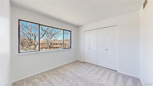 unfurnished bedroom with a textured ceiling, carpet, visible vents, and baseboards