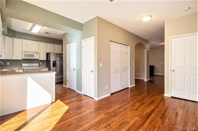 kitchen featuring white cabinets, stove, stainless steel fridge, and dark wood-type flooring