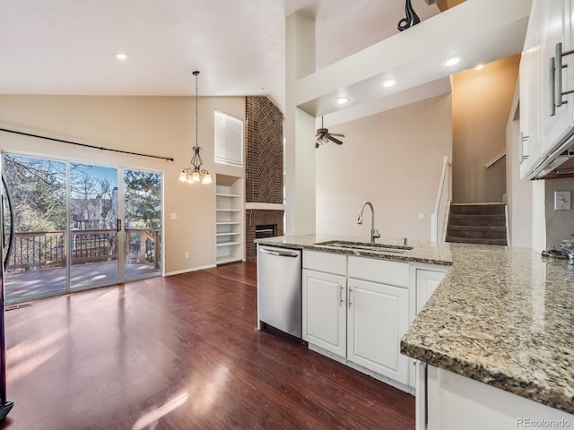 kitchen with dark wood-style floors, stainless steel dishwasher, a brick fireplace, a sink, and ceiling fan with notable chandelier