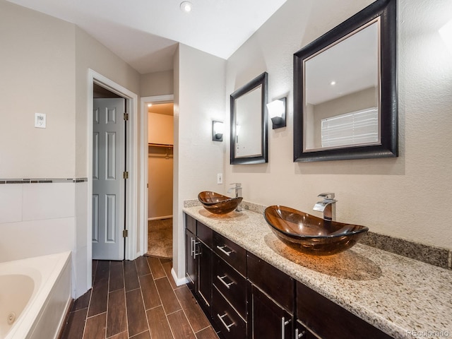 bathroom with a garden tub, a spacious closet, a sink, and wood finish floors