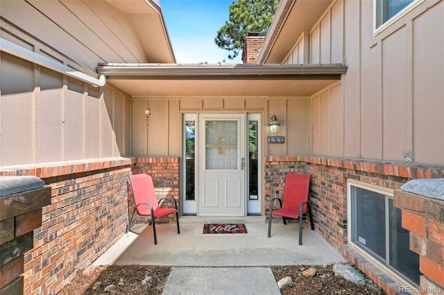 view of exterior entry with a porch, brick siding, board and batten siding, and a chimney