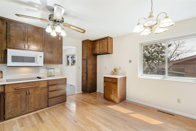 kitchen featuring visible vents, brown cabinets, light wood-style flooring, black electric stovetop, and white microwave