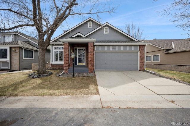 view of front of home featuring driveway, roof with shingles, a front yard, a garage, and brick siding