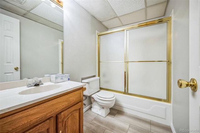 full bathroom featuring shower / bath combination with glass door, a drop ceiling, toilet, and vanity