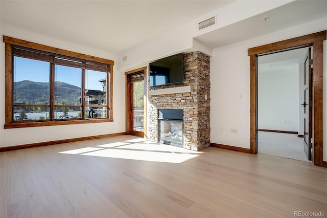 unfurnished living room with light hardwood / wood-style floors and a stone fireplace