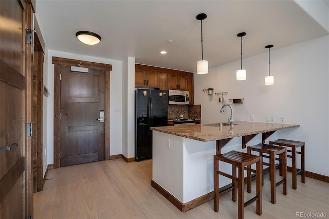 kitchen with kitchen peninsula, hanging light fixtures, black fridge, stone counters, and light hardwood / wood-style floors