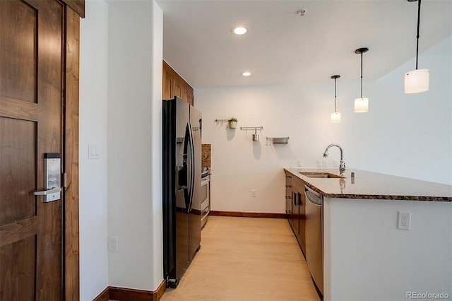 kitchen featuring black fridge, stainless steel dishwasher, light wood-type flooring, sink, and decorative light fixtures