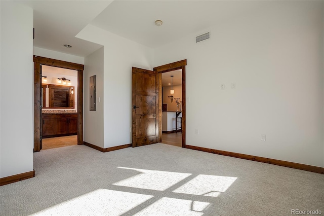 unfurnished bedroom featuring ensuite bathroom, electric panel, and light colored carpet