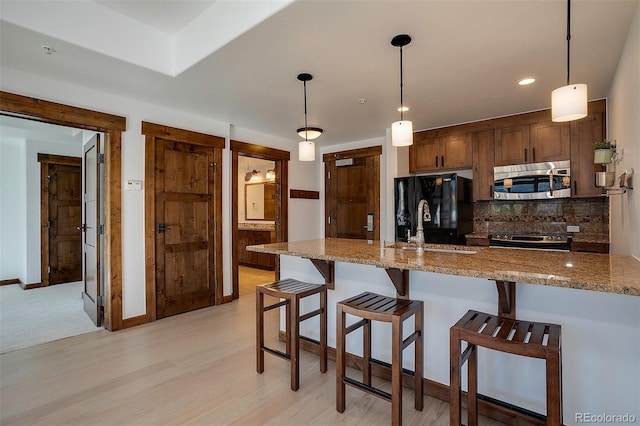 kitchen with decorative light fixtures, stainless steel appliances, sink, and light stone counters