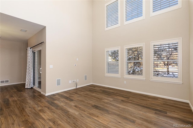 empty room featuring dark wood-type flooring and a towering ceiling