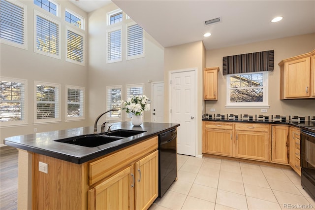 kitchen featuring sink, light tile patterned floors, light brown cabinets, an island with sink, and black appliances