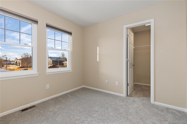 unfurnished bedroom with a walk in closet, light colored carpet, and a closet