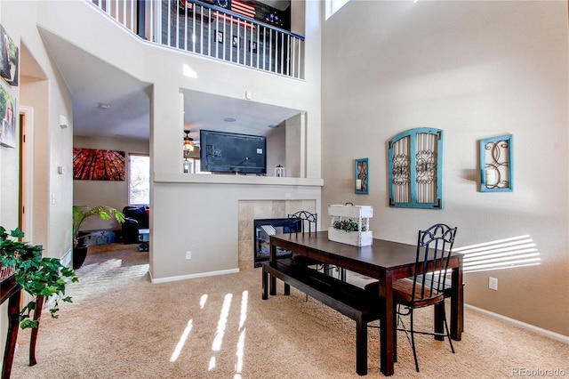 dining room featuring a tiled fireplace, light carpet, and a towering ceiling