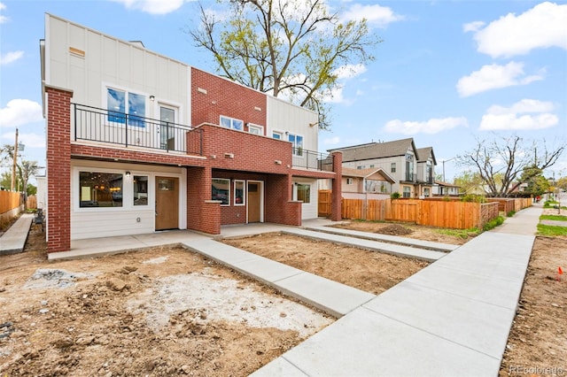 back of property with a balcony, board and batten siding, brick siding, fence, and a patio area