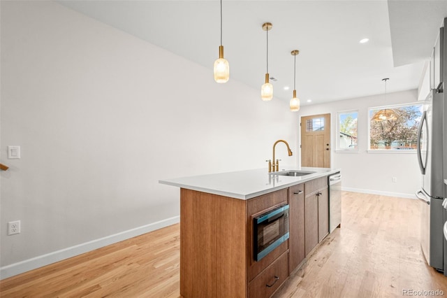 kitchen with a sink, light wood finished floors, stainless steel appliances, and baseboards