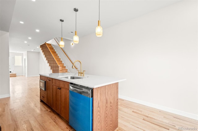 kitchen featuring dishwashing machine, a sink, light wood-type flooring, a center island with sink, and baseboards