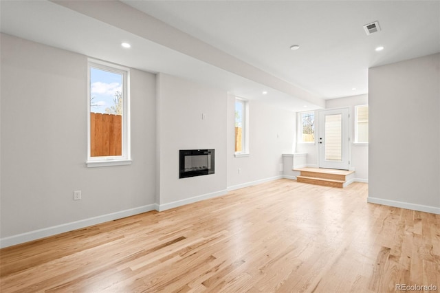 unfurnished living room with light wood-type flooring, baseboards, a glass covered fireplace, and visible vents