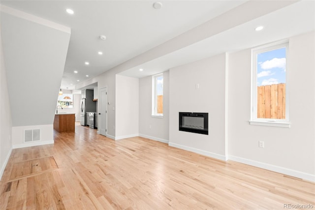 unfurnished living room featuring recessed lighting, light wood finished floors, a glass covered fireplace, and visible vents