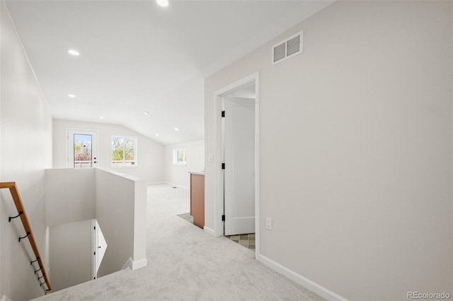 hallway featuring carpet flooring, an upstairs landing, visible vents, baseboards, and vaulted ceiling