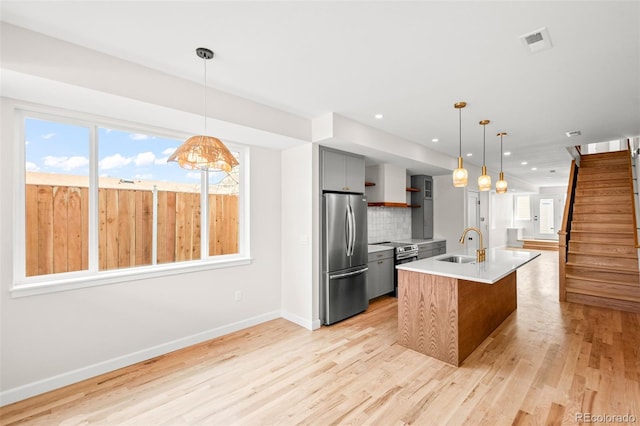 kitchen featuring appliances with stainless steel finishes, a sink, open shelves, light wood finished floors, and light countertops