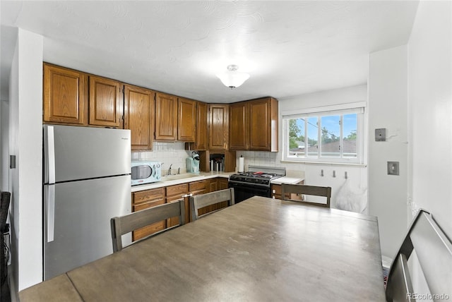 4505 W Gill Pl, Denver, CO 80219 - kitchen with freestanding refrigerator, black range with gas stovetop, decorative backsplash, and brown cabinetry