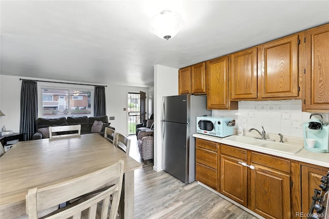 4505 W Gill Pl, Denver, CO 80219 - kitchen with freestanding refrigerator, white microwave, brown cabinets, light wood-type flooring, and light countertops