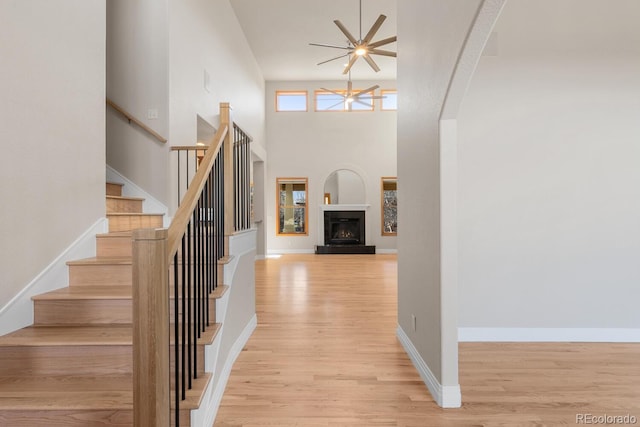 foyer entrance with wood finished floors, baseboards, a fireplace with raised hearth, ceiling fan, and stairs