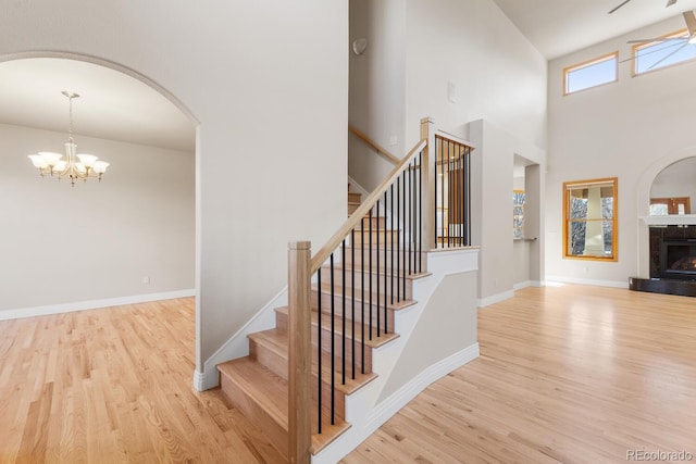 staircase with baseboards, arched walkways, a notable chandelier, and wood finished floors