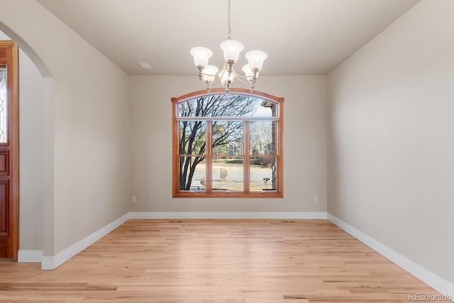 unfurnished dining area featuring light wood-type flooring, arched walkways, baseboards, and a chandelier