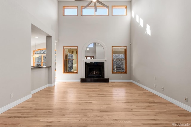 unfurnished living room with light wood finished floors, a fireplace, baseboards, and a towering ceiling