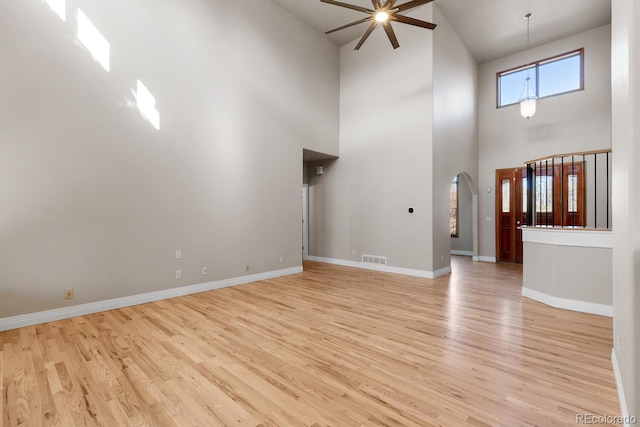 unfurnished living room with baseboards, visible vents, light wood-style flooring, arched walkways, and ceiling fan