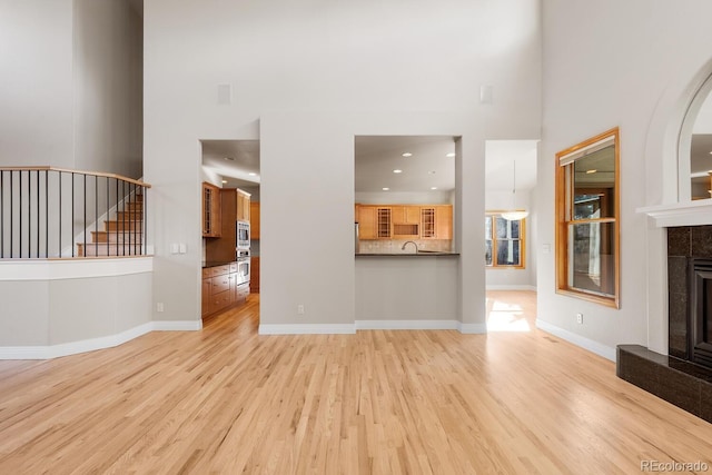 unfurnished living room with baseboards, a tiled fireplace, stairs, light wood-style floors, and a towering ceiling