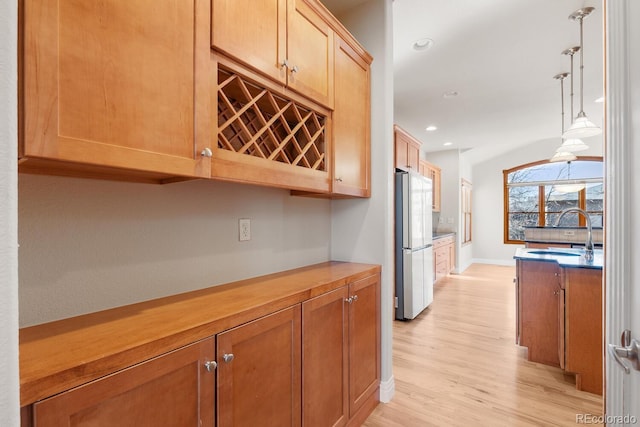 kitchen featuring recessed lighting, light wood-style flooring, freestanding refrigerator, hanging light fixtures, and a sink