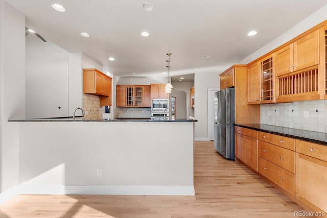 kitchen with arched walkways, a peninsula, stainless steel appliances, and glass insert cabinets